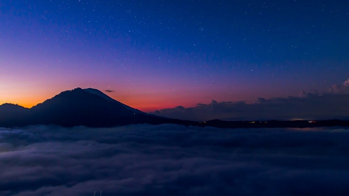 Mountain peak above clouds at twilight with stars