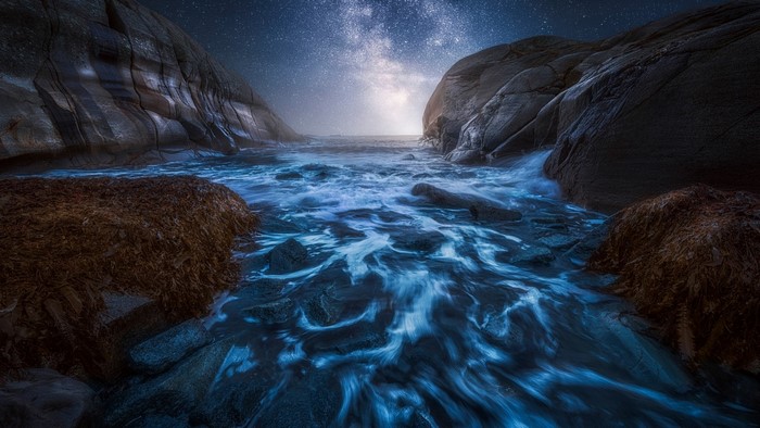 Ocean waves crashing between rocky cliffs under a starry sky