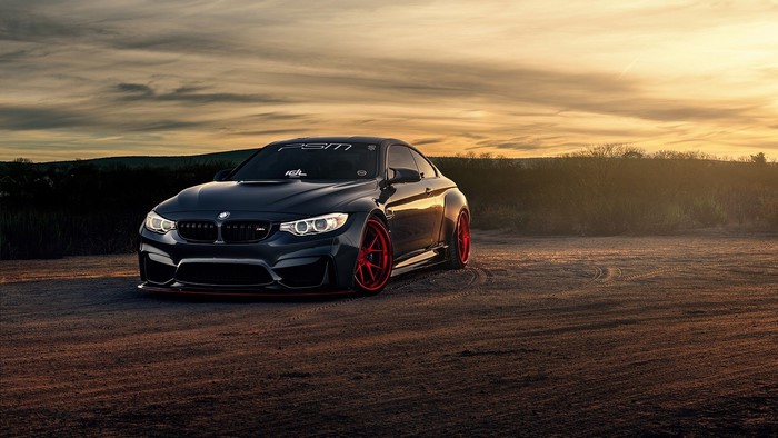 Dark BMW M4 with red wheels at sunset