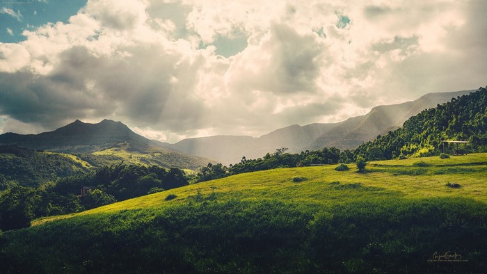 Sunlight beams through clouds over a green mountain landscape