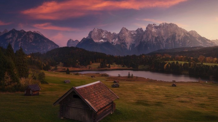 Wooden cabins by a lake with mountains at sunset