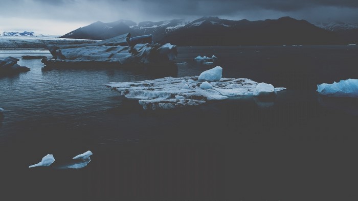 Icebergs floating in dark water with mountains in background