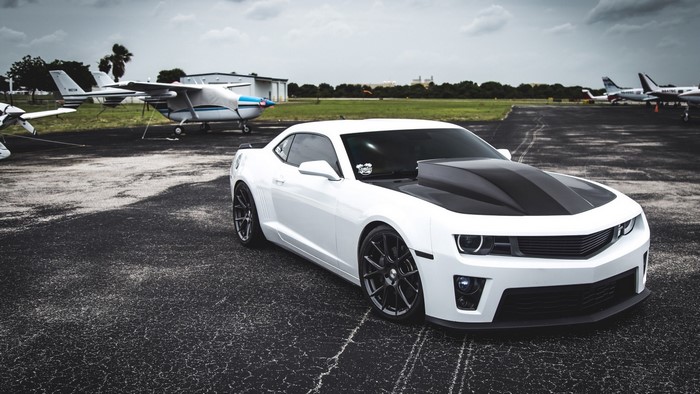 White Chevrolet Camaro with black hood at airport