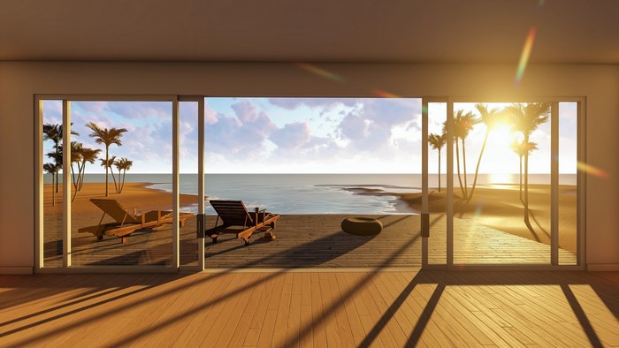Modern room with sliding glass doors overlooking a tropical beach at sunset