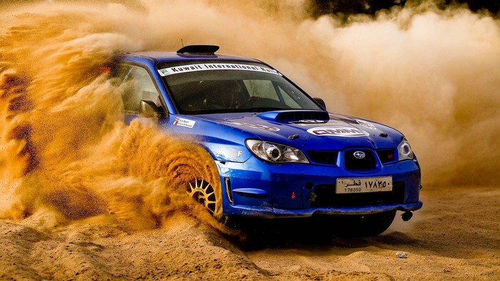 Blue Subaru Impreza STI rally car kicking up sand