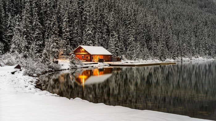 Log cabin by a snowy lake with pine forest reflection