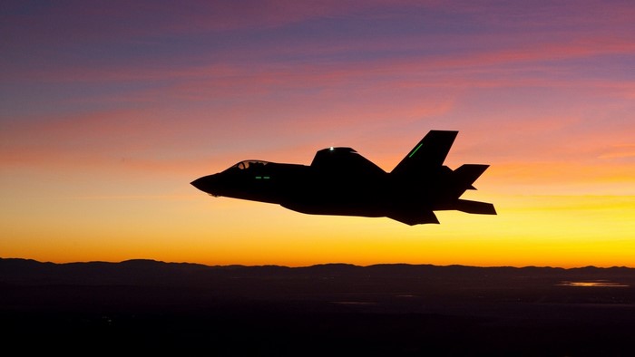Silhouette of an F-35A fighter jet in flight at sunset