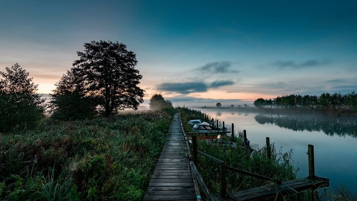 Wooden boardwalk along a misty lake at sunrise