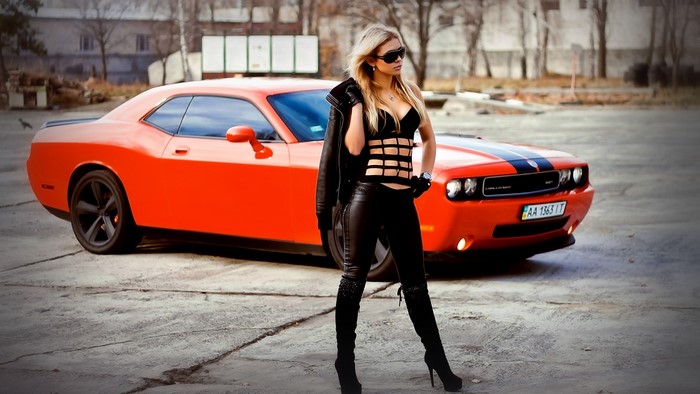 Woman in black outfit posing with orange Dodge Challenger