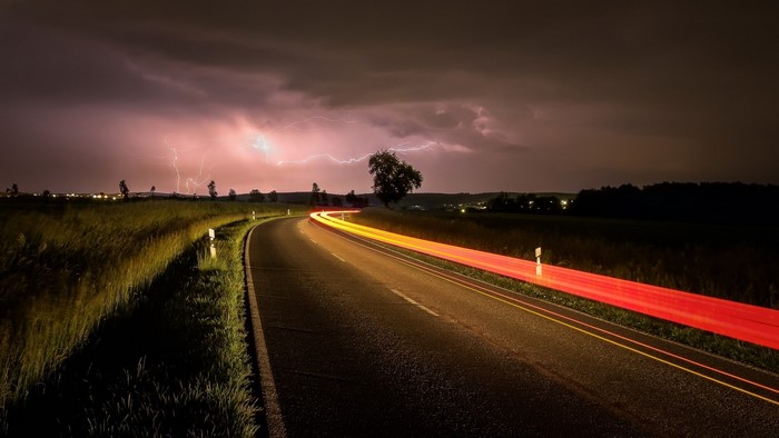 Road at night with lightning storm and light trails