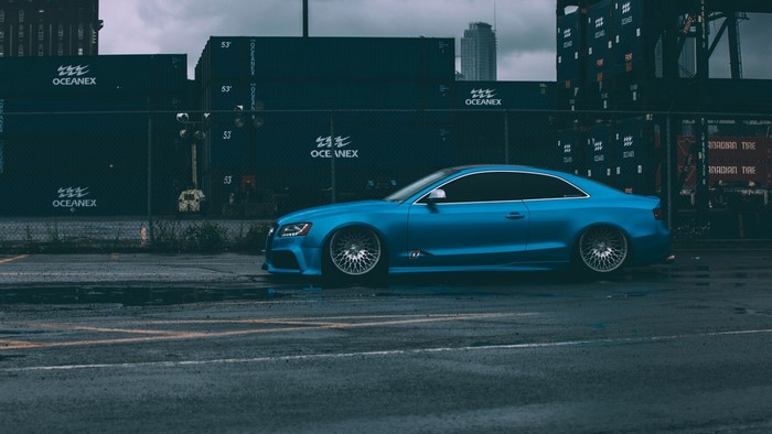 Blue Audi S5 parked near shipping containers