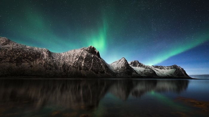 Aurora Borealis over snow-capped mountains reflected in a mirror river