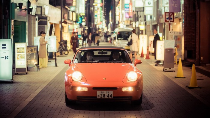 Orange Porsche driving in Tokyo at night
