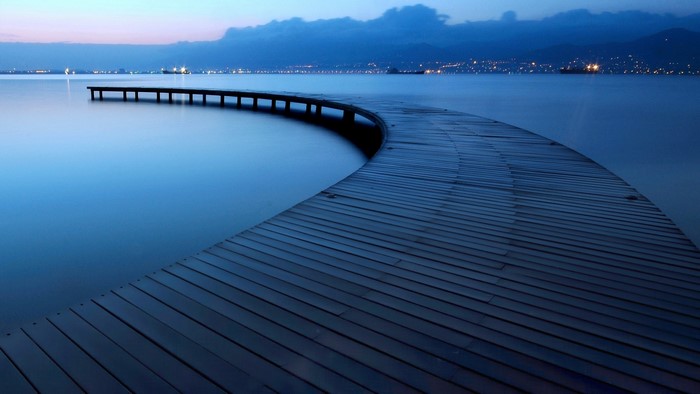 Curved wooden pier over calm blue water at dusk