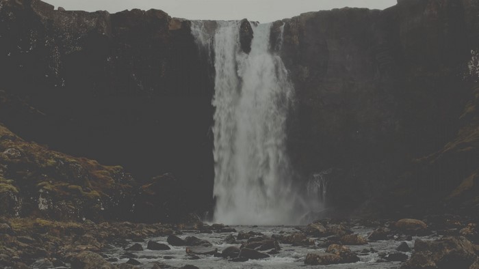 Waterfall cascading over dark cliffs into a rocky riverbed