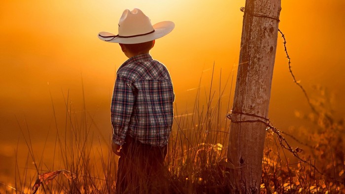 Little cowboy in a hat at sunset