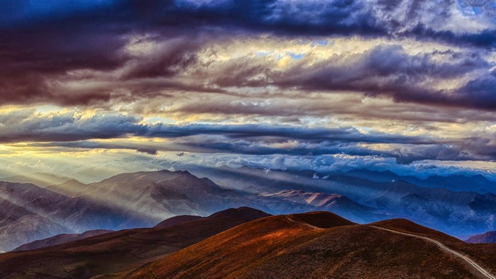 Sunbeams through dramatic clouds over mountain ranges