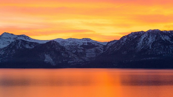 Snow-capped mountains reflected in a golden lake at sunset