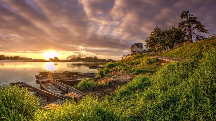 Boats on a river at sunrise with a house on the hill