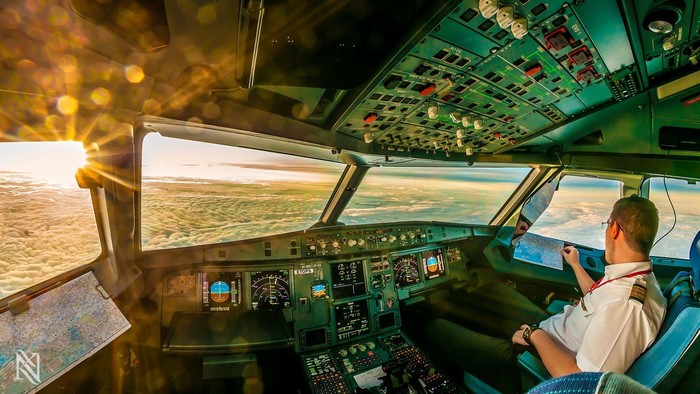 Pilot in cockpit flying above clouds at sunset