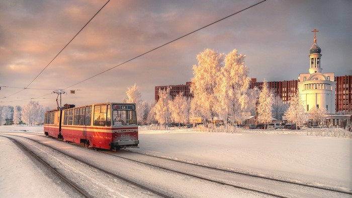 Red tram on snowy tracks near a church