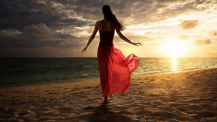 Girl in red dress on beach at sunset