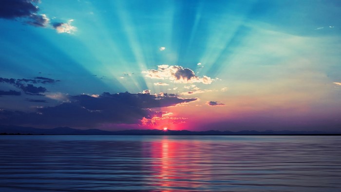 Sunlight Rays Over Calm Water at Sunset