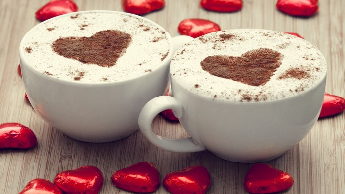 Two cups of coffee with heart art and chocolates
