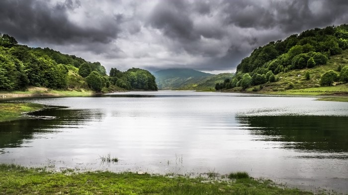 Lake surrounded by green hills under cloudy sky