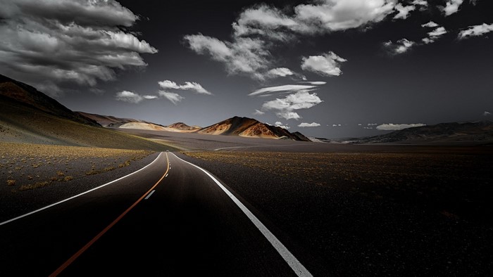 Road through a desolate landscape with mountains and clouds