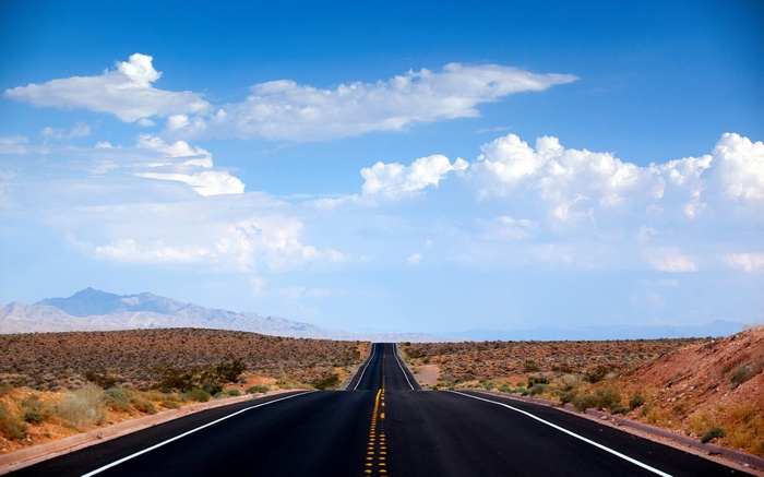 Desert highway stretching towards mountains under a cloudy sky
