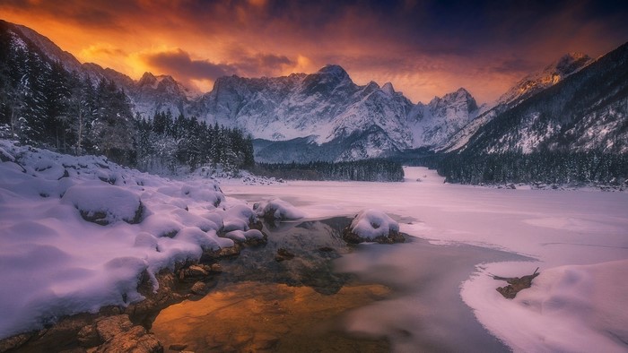Snowy mountains and frozen lake at sunset in Italy