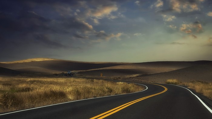 Winding road through rolling hills under cloudy sky