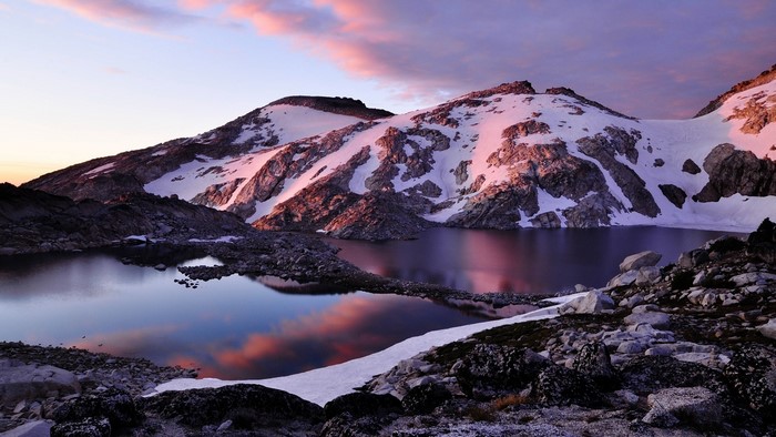Snow-capped mountains reflected in a lake at sunset
