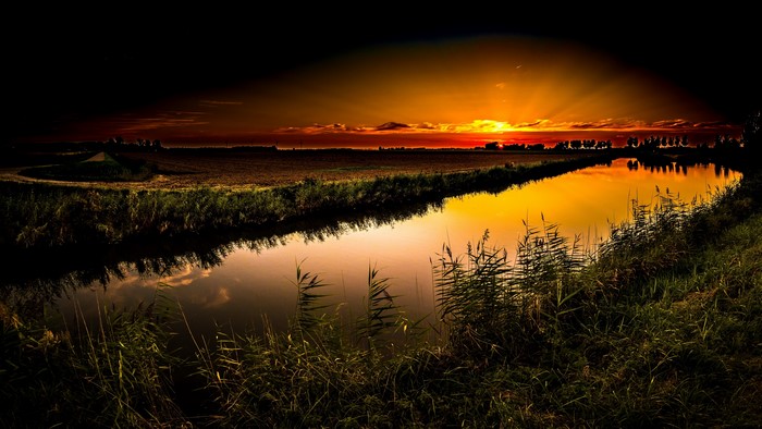 Sunset over a canal with reeds and fields