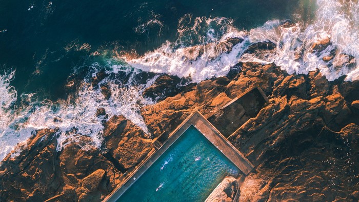 Aerial view of ocean waves crashing on rocks near a swimming pool