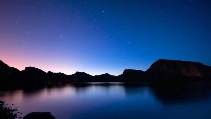 Night sky over a lake with mountain reflections
