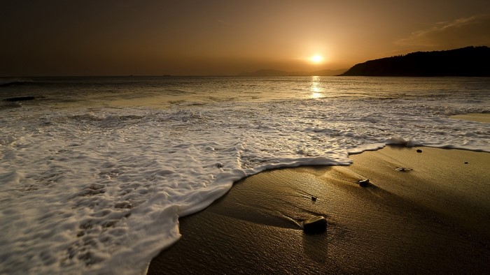 Sunset over a beach with waves and a hill