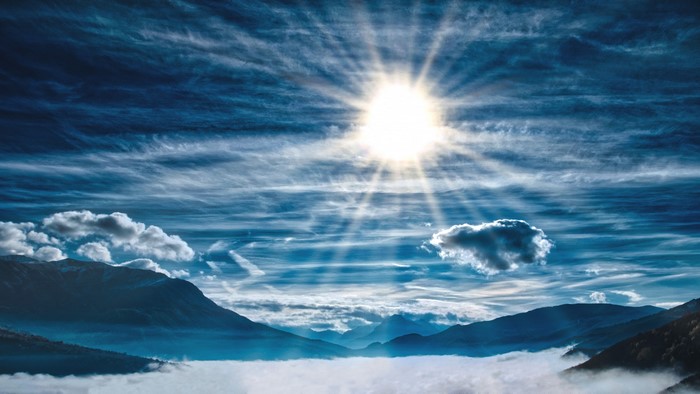 Sun shining through clouds over mountains