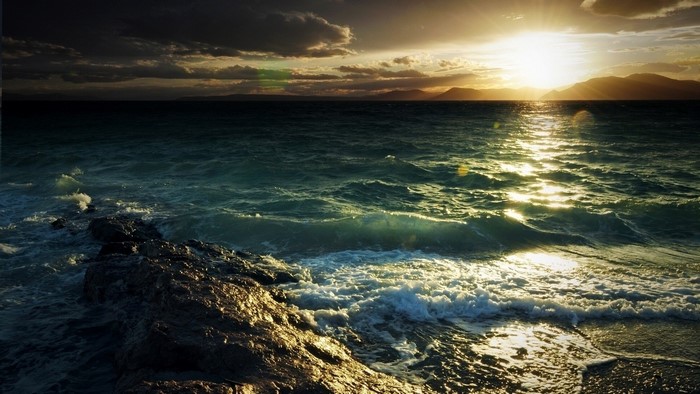 Ocean waves crashing on rocky shore at sunset