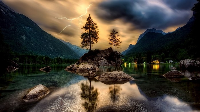 Lightning strikes over a lake with trees on a rocky island