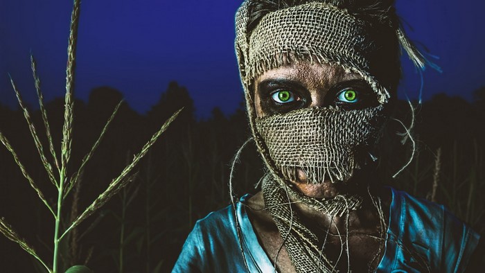 Scarecrow with glowing green eyes in a cornfield at night