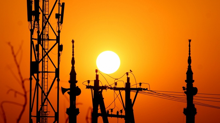 Silhouette of cell towers and power lines against a sunset