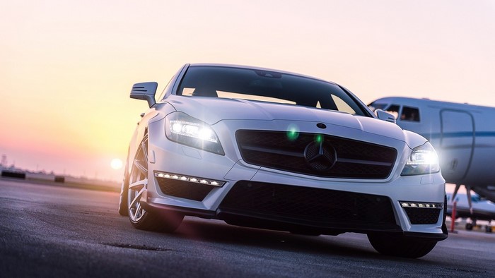White Mercedes-Benz CLS parked by a private jet