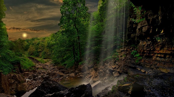 Waterfall in a lush green forest with a dramatic sky