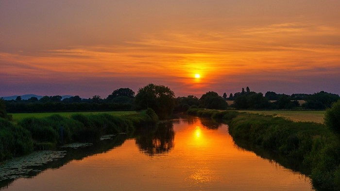 Sunset over a river with trees and fields