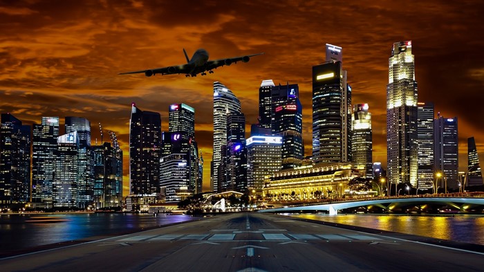 Airplane flying over Singapore skyscrapers at sunset