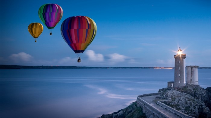 Hot air balloons over the sea at dusk with a lighthouse