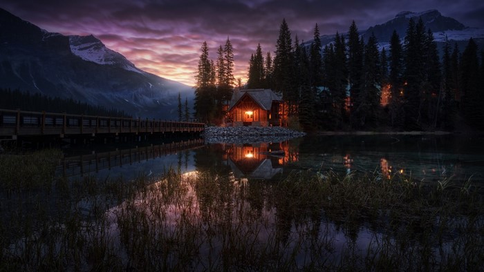 Cabin by a lake at sunset with mountains