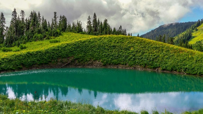 Turquoise mountain lake surrounded by green hills and pine trees